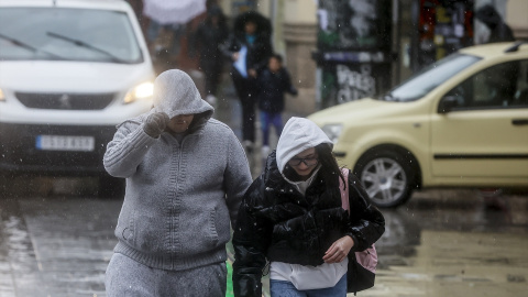 Foto de archivo de dos personas tapándose la cabeza con la capucha de la chaqueta como consecuencia de la lluvia