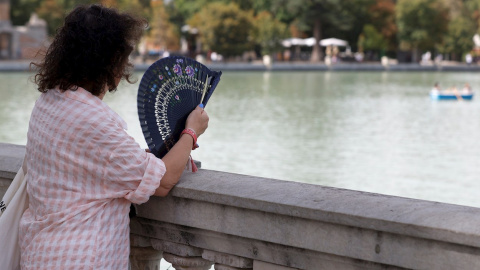 Una mujer combate el calor con un abanico mientras observa el lago del Parque del Retiro de Madrid.