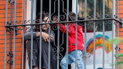 Una joven y un niño asomados entre las rejas de una ventana de una vivienda. EFE/José Manuel Vidal/Archivo