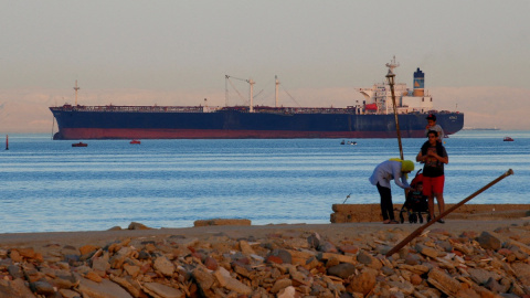 La gente camina por la playa mientras un barco portacontenedores cruza el Golfo de Suez hacia el Mar Rojo antes de ingresar al Canal de Suez.