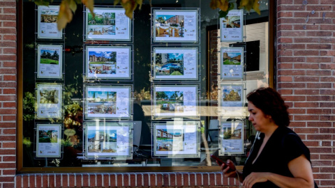 Una mujer camina frente a un escaparate de anuncios de viviendas, a 4 de agosto de 2023, en Madrid.