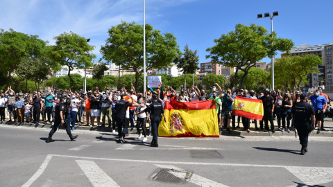 Varias personas se concentran con carteles y banderas de España frente al coche del presidente del Gobierno y el ministro de Interior , a su llegada al Helipuerto de Ceuta, a 18 de mayo de 2021, en Ceuta (España).