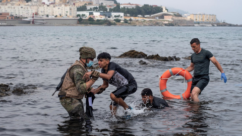 Un soldado del Ejército ayuda a dos migrantes a salir del agua en la playa de El Tarajal este miércoles 19 de mayo de 2021.