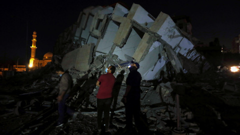 Varios palestinos en el lugar donde un edificio fue destruido por los ataques aéreos israelíes en medio de un estallido de violencia israelí-palestina