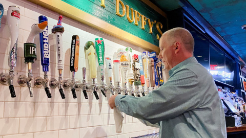 17/05/2021. Imagen de archivo del dueño del bar Pat Hughes limpiando los grifos de cerveza, en Nueva York. - REUTERS