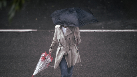 Una persona camina bajo la lluvia protegida con un paraguas, en Madrid (España).