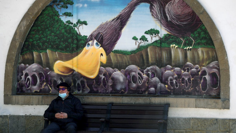 Un hombre con mascarilla sentado ante un grafiti de la Biblioteca Pública del Parque de San Francisco en el centro de Oviedo.