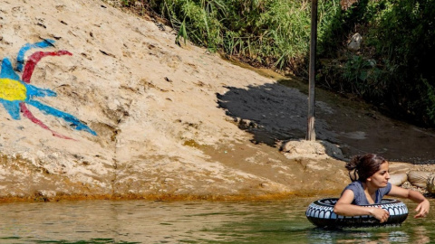 Una joven asiria se baña en el valle de Nahla junto a la bandera del movimiento nacional asirio. Es una descendiente de los supervivientes del genocidio. Foto por Ferran Barber