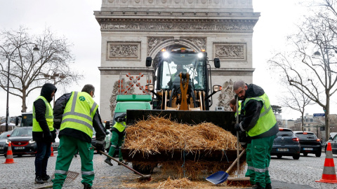 Los trabajadores municipales limpian paja arrojada por un tractor frente al Arco del Triunfo, en París, tras una protesta del sector agrario francés.