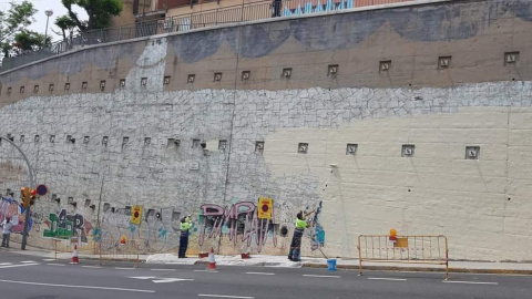 Operaris de BCNeta esborren el mural del tauró capitalista al barri del Carmel.