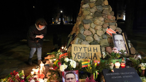 Una mujer se agacha para encender una vela, mientras la gente asiste a un evento conmemorativo, después de la muerte del líder de la oposición rusa Alexei Navalny en Vilna, Lituania.