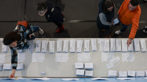 Varias personas escogen papeletas para ejercer su derecho al voto en el pabellón polideportivo Ames en A Coruña durante la jornada electoral en Galicia, este domingo.