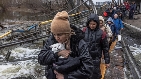 Una mujer con su gato cruza un puente destruido mientras los residentes huyen desde el frente de la ciudad de Irpín, en Kiev, este lunes 7 de marzo de 2022.