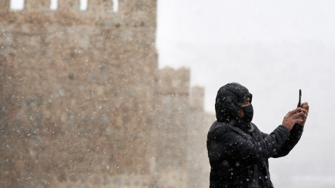 Un hombre se hace una foto con su teléfono móvil junto a la muralla de Ávila durante la primera nevada del otoño en la capital abulense.