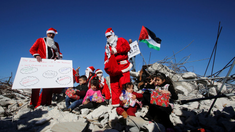 Jóvenes vestidos de Papa Noel junto a varios niños en los escombros de una casa palestina demolida por fuerzas israelíes en Bethlehem, Cisjordania. - REUTERS