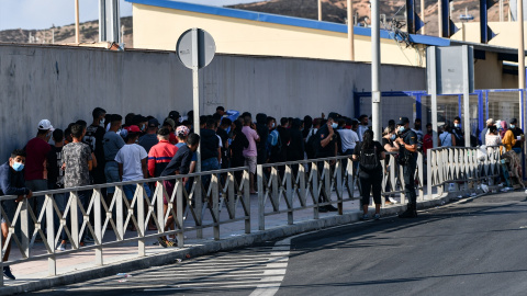 Agentes de Policía supervisan a cientos de personas, la mayoría marroquíes, que guardan cola en la oficina para tramitar los asilos situada en la frontera del Tarajal que separa Ceuta de Marruecos, a 3 de agosto de 2021, en Ceuta (España). Imagen de a