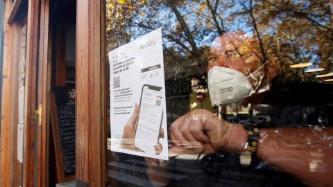 El responsable de un bar del barrio de Gracia de Barcelona cuelga un cartel avisando a sus clientes de la necesidad de presentar el certificado de vacunación para entrar en el local.