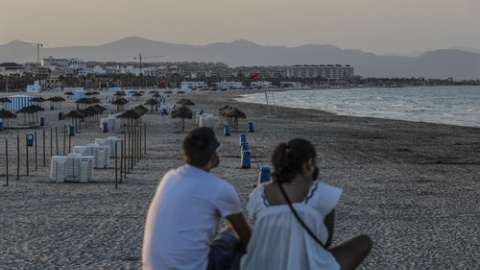 Dos jóvenes sentados contemplan la playa de la Malvarrosa durante la noche de San Juan en Valencia