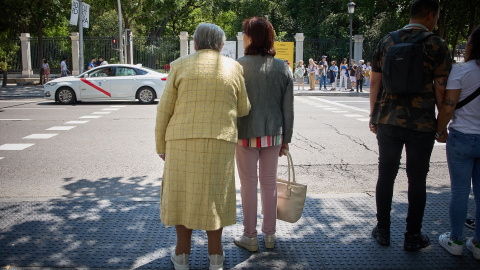 Una mujer mayor espera para cruzar una calle, con ayuda, por el centro de Madrid, a 4 de junio de 2023.