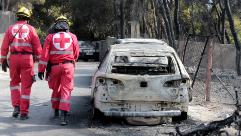 Miembros de la Cruz Roja caminan junto a un vehículo calcinado en una zona afectada por los incendios en Argyra Akti, en Mati (Grecia).  EFE/Pantelis Saitas