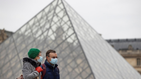 Peatones con mascarillas caminan junto a la pirámide del Louvre, este jueves en París.