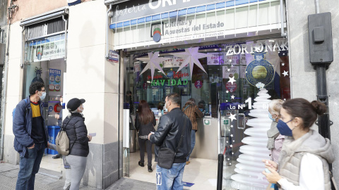 Personas hacen cola y compran décimos de lotería de navidad este martes en una administración de lotería en Bilbao.