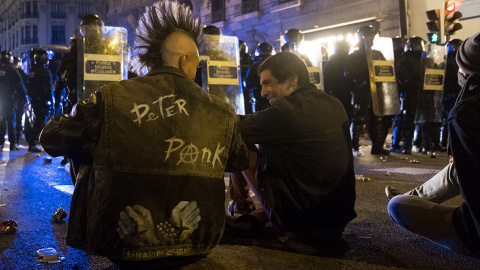 Dos jóvenes manifestantes hablan distendidamente mientras están sentados en primera línea de la barrera frente a los antidisturbios de los Mossos en Urquinaona. GUILLEM SANS.