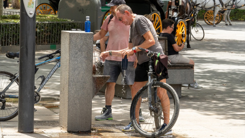 22/07/2024 Unos turistas junto a una fuente de agua pública en Sevilla. Imagen de archivo.