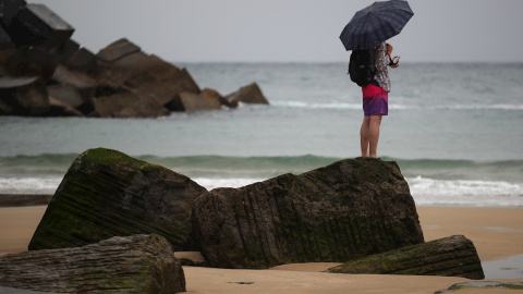 Un joven se protege con un paraguas en la playa de la Zurriola de San Sebastián.