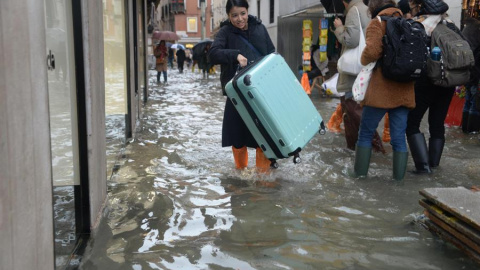 Una turista carga su maleta con ruedas para evitar que toque el "agua alta" en Venecia (Italia), este viernes. EFE/Andrea Merola