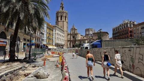 Varias turistas pasean por el asfaltado levantado y las vallas que rodean completamente la céntrica plaza de la Reina de València por las obras que se llevan a cabo para remodelarla.