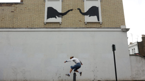 Un joven pasa con su skateboard delante de la pintada del artista callejero Banksy, in el barrio londinense de Fulham. REUTERS/Mina Kim