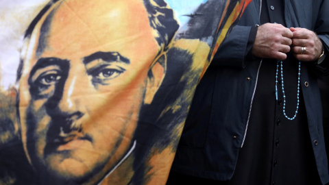 Un sacerdote sostiene un rosario junto a una bandera con el retrato del dictador Francisco Franco afuera del cementerio Mingorrubio-El Pardo. REUTERS / Sergio Perez