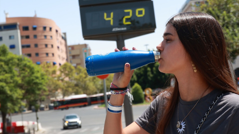 14/08/2024 Una joven bebe agua en la calle en Sevilla este agosto. Al fondo, un termómetro.