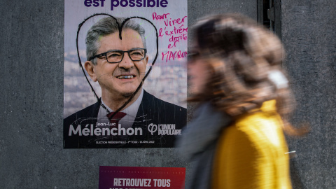 Una mujer camina en París el 9 de abril de 2022 frente a un cartel de campaña de La Francia Insumisa (LFI), partido liderado por Jean-Luc Mélenchon.