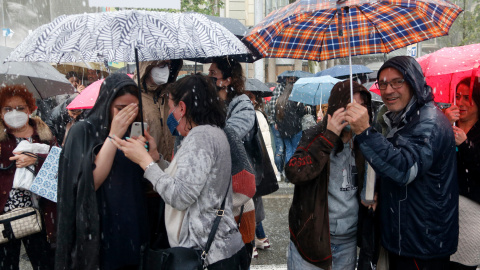 Diverses persones sota la pedregada davant les parades de llibres de Barcelona.