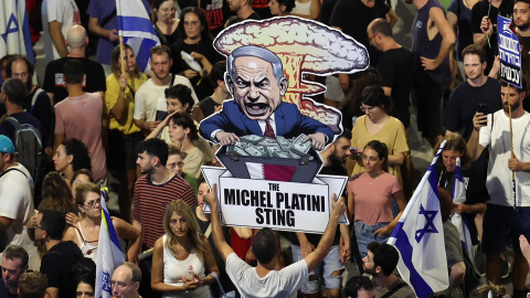 Un manifestante sostiene un cartel con una caricatura del primer ministro israelí, Benjamin Netanyahu, en el que se puede leer "La trampa de Michel Platini", mientras miles de manifestantes que apoyan a las familias de los rehenes israelíes retenidos po