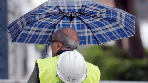 Un trabajador de la construcción se protege de la lluvia con un paraguas en Valencia. EFE/Kai Försterling