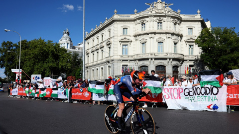 Un ciclista del equipo Jayco AlUla pasa junto a personas con banderas y pancartas en apoyo a los palestinos en Gaza, en la última etapa de la Vuelta a España, en la madrileña Plaza de Cibeles