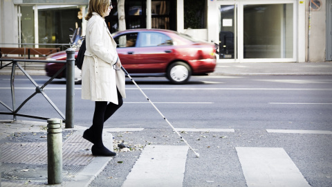 Una persona con discapacidad visual cruzando un paso de peatones ayudándose con un bastón. / ONCE