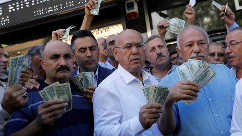 Varias personas sostiene billetes de dólar delante de una oficina de cambio em Ankara, respondiendo a la llamada del presidente Erdogan a cambiar billetes verdes par sostener la lira turca. REUTERS/Umit Bektas