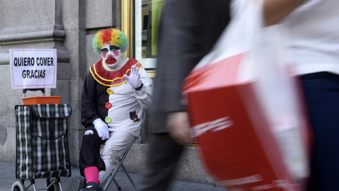 Rayito, un mendigo disfrazado de payaso, saluda sentado junto a un cartel que dice "Quiero comer, gracias" en la calle Gran Vía, en el centro de Madrid, el 28 de octubre de 2014.