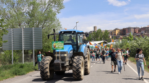 Un dels tractors participants a la mobilització en contra dels Jocs d'hivern 2030, convocada per la Plataforma Stop JJOO, sortint de la zona industrial de Puigcerdà amb la capçalera de la marxa al darrere i on es veu els edificis de la localitat al fon