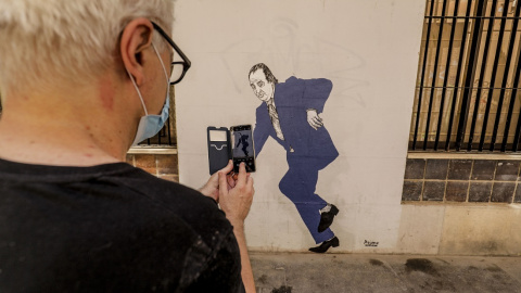 Un hombre hace una fotografía con su móvil al graffiti del rey emérito Juan Carlos I tropezando y a punto de caer, obra pintada en una céntrica calle de Valencia por el artista gallego apodado 'el Primo de Banksy', en Valencia, Comunidad Valenciana (E