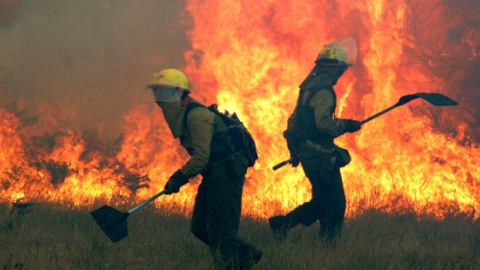 Fotografía de archivo de dos bomberos intentando controlar un incendio forestal en Galicia. EFE