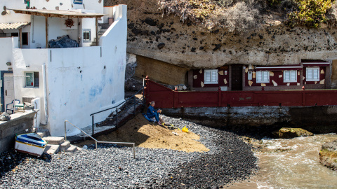 Dos personas disfrutan de la playa en el Puertito de Adeje junto a una de las 22 viviendas de la localidad