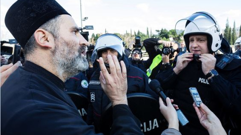 Un sacerdote de la Iglesia Ortodoxa Serbia habla con un policía antidisturbios en un puente cerca del parlamento, antes de votar un proyecto de ley sobre "Libertades religiosas y derechos legales de las organizaciones religiosas" en Podgorica | Reuters