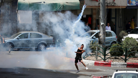 Los manifestantes palestinos devuelven un bote de gas lacrimógeno en medio de los enfrentamientos durante las protestas contra la 'Marcha de la bandera' anual en Jerusalén, en la ciudad cisjordana de Hebrón, el 29 de mayo de 2022.