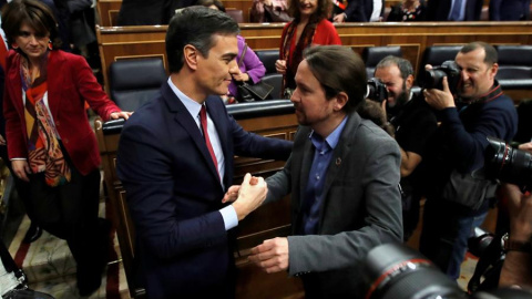 El líder de Unidas Podemos, Pablo Iglesias (d), felicita a Pedro Sánchez, quien logró este martes la confianza del Congreso para un nuevo mandato como presidente del Gobierno, al lograr una estrecha mayoría de 167 votos a favor, 165 en contra y 18 abs