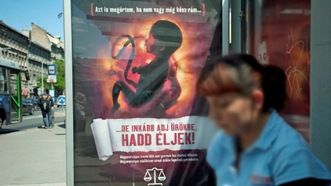 Una mujer espera junto a un cartel antiaborto con la imagen de un feto y el lema 'Puedo entender si aún no estás preparado para recibirme, ¡pero haz que me adopten y déjenme vivir!', en Budapest, a 17 de mayo de 2011.